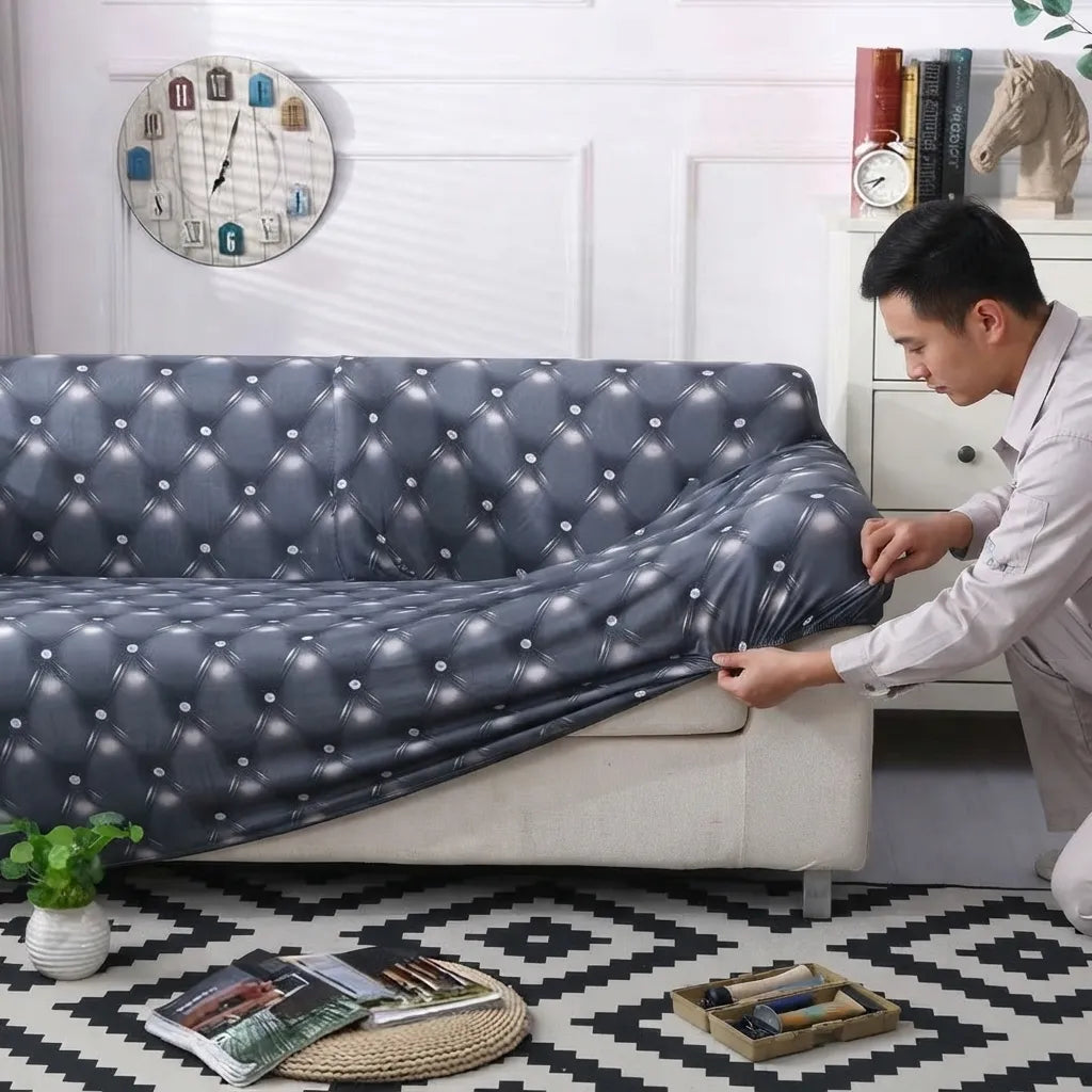 A man in a white shirt is shown pulling a dark gray tufted sofa slipcover onto a light beige sofa in a decorated living room setting.