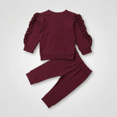 A two-piece children's outfit in deep burgundy, featuring a long-sleeve top with dramatic ruffled flutter sleeves and matching jogger pants, laid flat on a light gray background.
