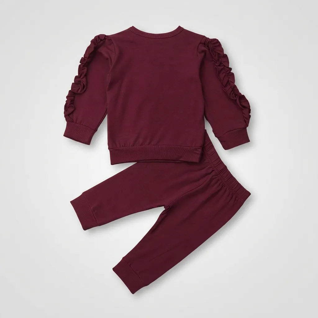 A two-piece children's outfit in deep burgundy, featuring a long-sleeve top with dramatic ruffled flutter sleeves and matching jogger pants, laid flat on a light gray background.