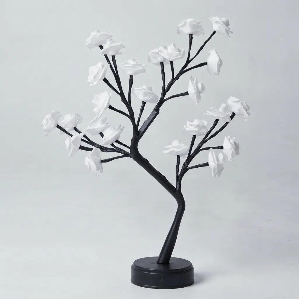 A decorative artificial flowering tree with black branches and white blossoms on a round black base, photographed against a plain light gray studio background.