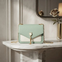 A mint green and white leather shoulder bag with a gold chain strap and a cat-shaped clasp, displayed on a white marble console table in a styled interior setting.