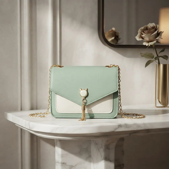 A mint green and white leather shoulder bag with a gold chain strap and a cat-shaped clasp, displayed on a white marble console table in a styled interior setting.