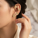 A close-up of a woman's ear wearing four gold butterfly-shaped stud earrings, with her hand gently touching her hair. The background is a soft, out-of-focus light beige.