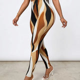 A model wearing high-waisted leggings with an abstract wavy pattern in tan, beige, brown, black, and off-white, paired with clear high-heeled mules against a plain studio background.