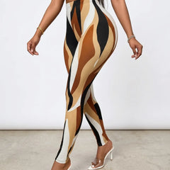 A model wearing high-waisted leggings with an abstract wavy pattern in tan, beige, brown, black, and off-white, paired with clear high-heeled mules against a plain studio background.