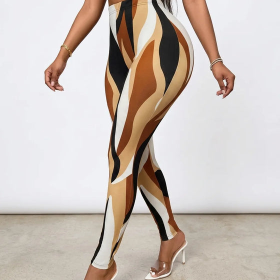 A model wearing high-waisted leggings with an abstract wavy pattern in tan, beige, brown, black, and off-white, paired with clear high-heeled mules against a plain studio background.