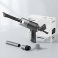 A handheld cordless vacuum cleaner in dark gray and black, shown with its white retail box and several included attachments on a clean light gray studio background. The box reads 'NO.