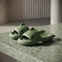 A pair of olive green shark slide sandals resting on a speckled stone countertop in a modern interior setting.