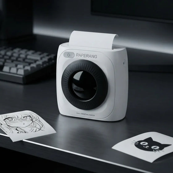 A compact white Paperang portable printer with a black circular lens area sits on a dark desk, with printed sheets and a blurred keyboard in the background.
