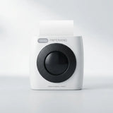 A Paperang instant camera-style printer in white with a large black circular lens area and a sheet of white paper emerging from the top, shown on a clean light gray studio background.