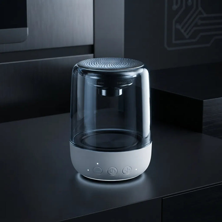 A modern cylindrical portable speaker with a clear glass upper chamber and a white control base, set on a dark glossy countertop in a sleek kitchen environment.