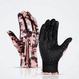 A pair of winter gloves shown front and back on a clean white background. One glove displays a pink, brown, and white digital camouflage pattern with a zipper, while the other shows a black textured palm with matching camouflage edges.
