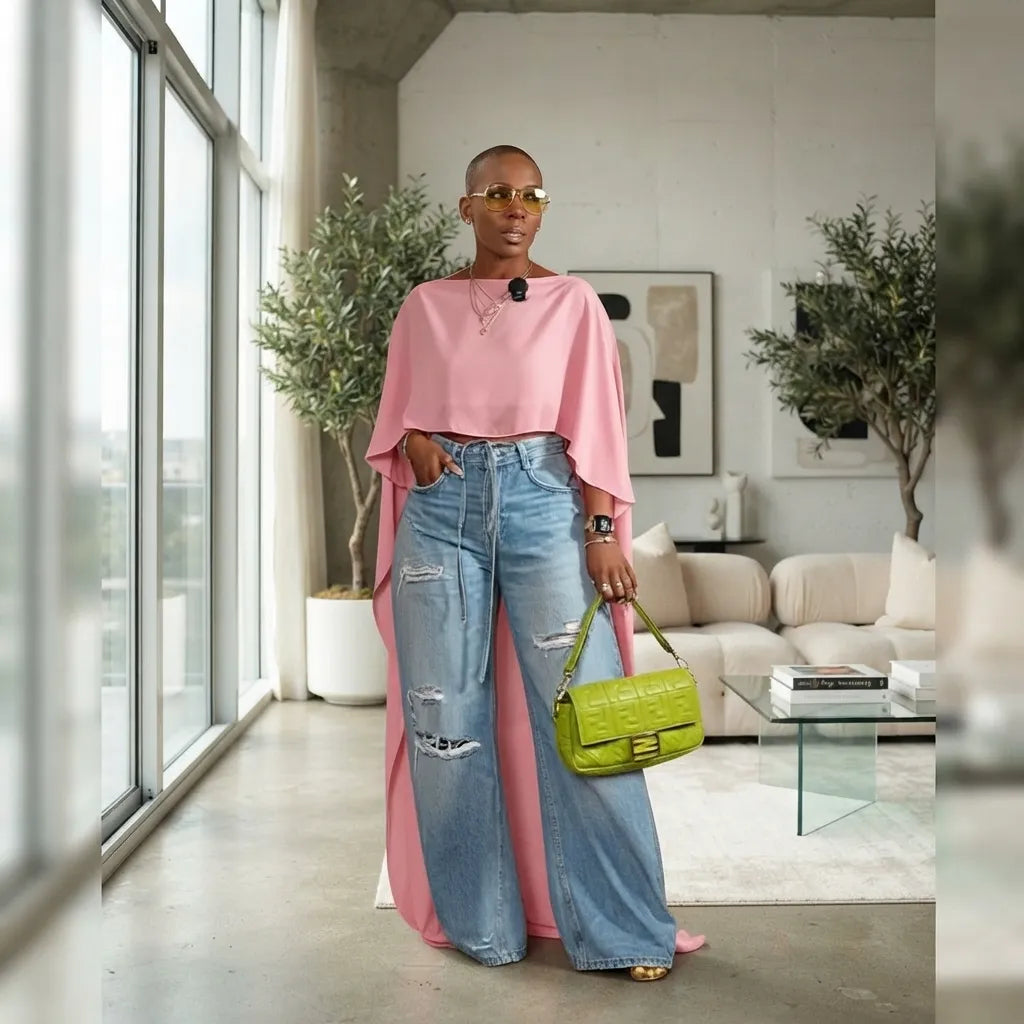 A woman stands in a modern living room wearing a pink draped top, light-wash distressed wide-leg jeans, and carrying a bright green handbag.