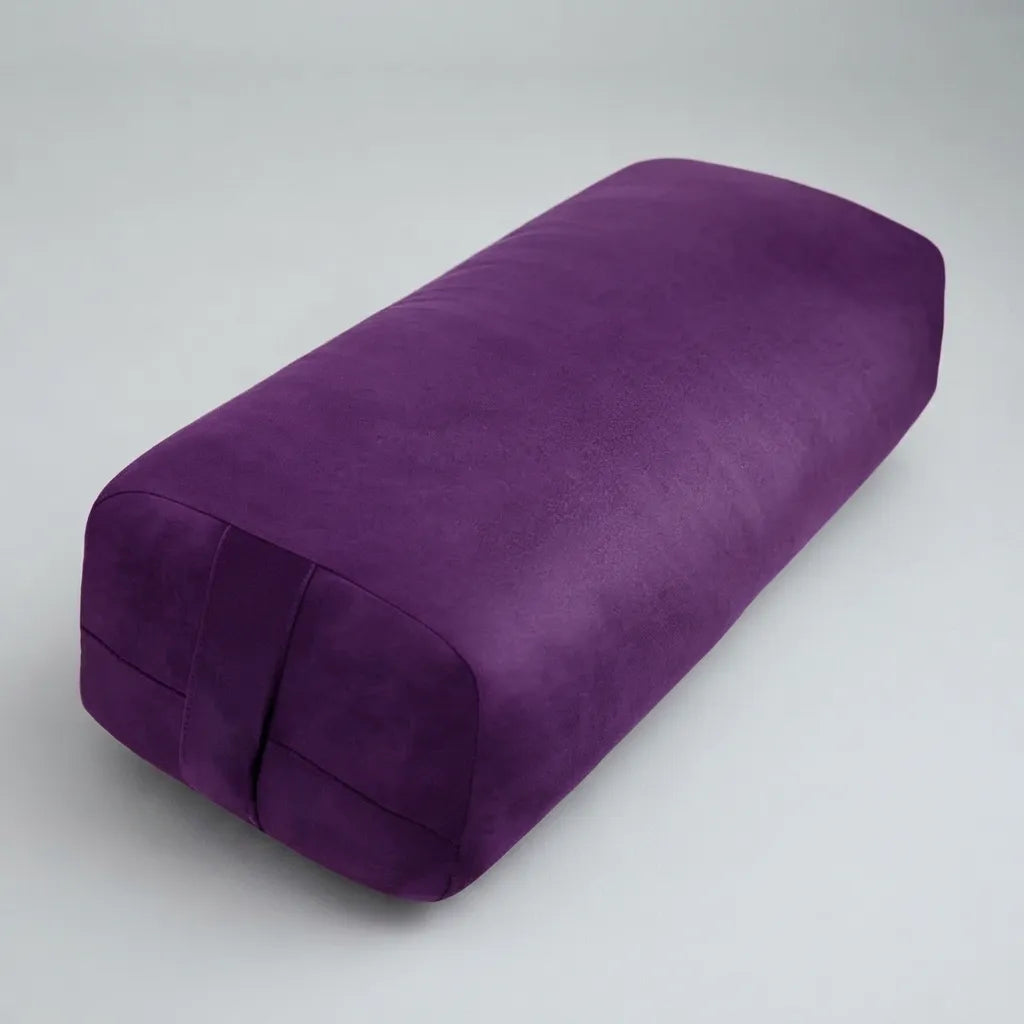 A purple cylindrical yoga bolster pillow with a textured fabric surface, shown on a neutral light gray background.