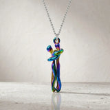 A silver ball-chain necklace with an abstract, swirling pendant in a metallic iridescent finish that shifts between blue, green, purple, and gold, displayed on a light textured surface.