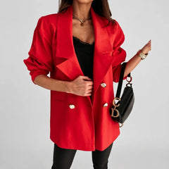 A woman wearing a bright red double-breasted blazer with gold buttons over a black top and black pants, holding a black handbag with gold hardware against a light gray studio background.