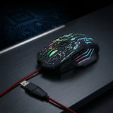 A black gaming mouse with vibrant RGB rainbow lighting and a red cable, resting on a dark desk surface.
