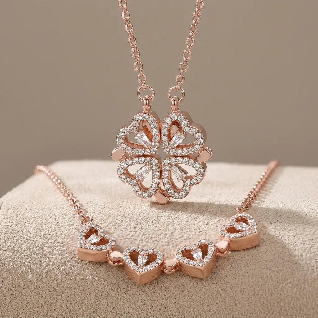 Rose gold jewelry set featuring a four-leaf clover pendant necklace and a matching heart-link bracelet, both adorned with clear rhinestones, displayed on a textured beige surface.