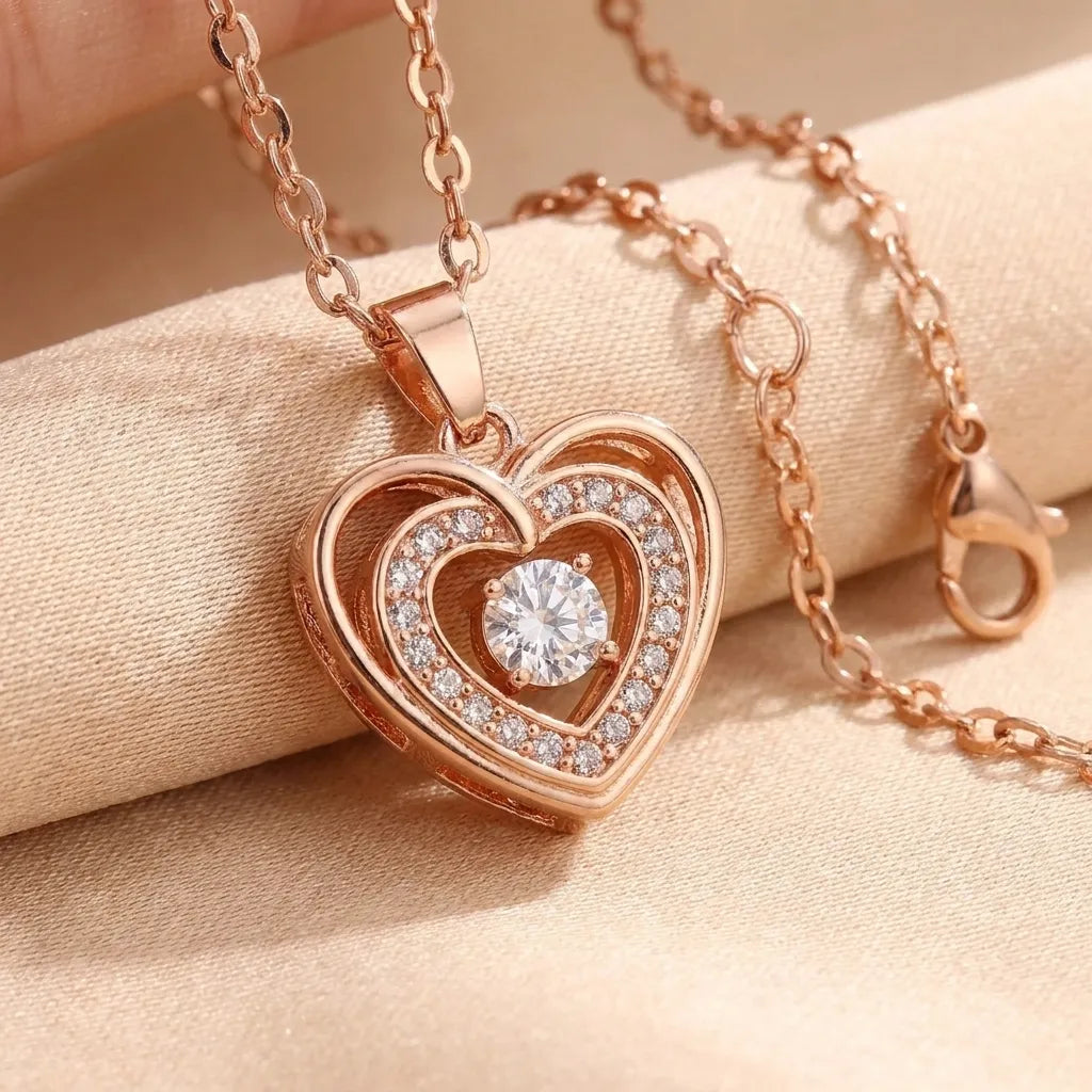 Rose gold heart-shaped pendant necklace with a clear central gemstone and small clear accent stones, displayed on a beige fabric surface.