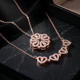 Rose gold necklace set featuring a floral clover pendant and a heart-link chain, displayed on a black marble surface.