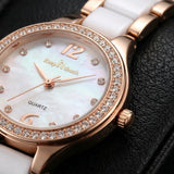 Close-up of a women's quartz watch with a white ceramic strap, white mother-of-pearl dial, rose gold case, crystal-encrusted bezel, and gold-tone 'Keep N touch' branding.