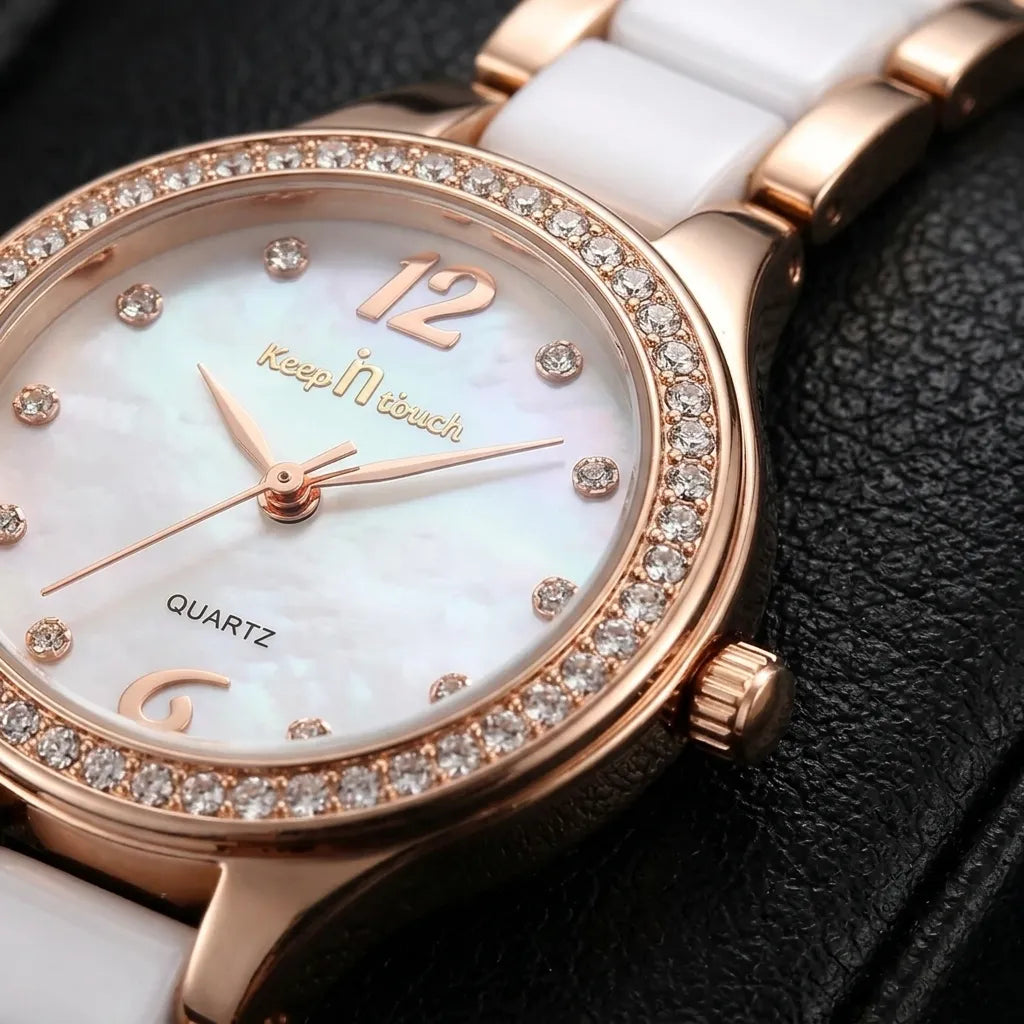 Close-up of a women's quartz watch with a white ceramic strap, white mother-of-pearl dial, rose gold case, crystal-encrusted bezel, and gold-tone 'Keep N touch' branding.