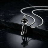 A silver-toned metal pendant necklace featuring an abstract, stylized human figure holding a heart, displayed on a black marble surface with a matching chain.