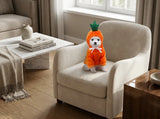 A small white dog wearing an orange carrot costume sits on a beige armchair in a modern living room setting.
