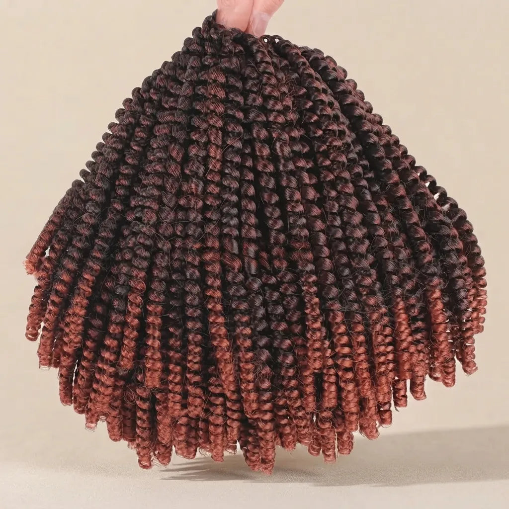 A hand holds up a large bundle of coiled twist braids with a dark brown to coppery reddish-brown ombré color gradient, set against a plain beige background.