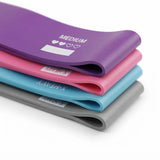 Four resistance bands stacked diagonally on a white background, showing purple, pink, light blue, and gray colors with white printed text indicating weight levels.