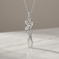A silver pendant necklace featuring a stylized dancing couple, suspended from a delicate silver chain and resting on a light marble surface against a neutral beige background.