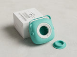 A mint green portable coffee maker with a matching lid, shown next to its white product box on a light gray surface.