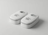 Two small white rectangular containers with rounded corners, shown on a light gray studio background. Each container has a gray paw print graphic on the lid and a circular clear window near the top.