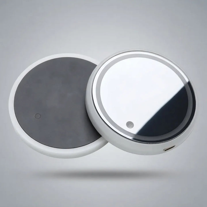 Two round electronic devices, likely wireless charging pads or smart home accessories, shown floating against a neutral gray background. One device displays a dark gray top surface, while the other shows a reflective silver and white top with a small circular cutout.