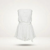 A white strapless romper with a ruffled neckline, a matching fabric tie belt at the waist, and a ruffled hem, shown floating against a light off-white background.