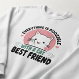 A white crewneck sweatshirt featuring a graphic print of a cute white cartoon cat inside a pink circle, with the text 'EVERYTHING IS POISABLE WITH A CAT BEST FRIEND' in black and teal lettering.