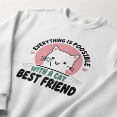 A white crewneck sweatshirt featuring a graphic print of a cute white cartoon cat inside a pink circle, with the text 'EVERYTHING IS POISABLE WITH A CAT BEST FRIEND' in black and teal lettering.