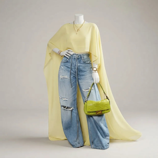 A mannequin styled in a pale yellow draped top, light-wash distressed wide-leg jeans, gold jewelry, and holding a bright yellow-green handbag against a neutral studio background.